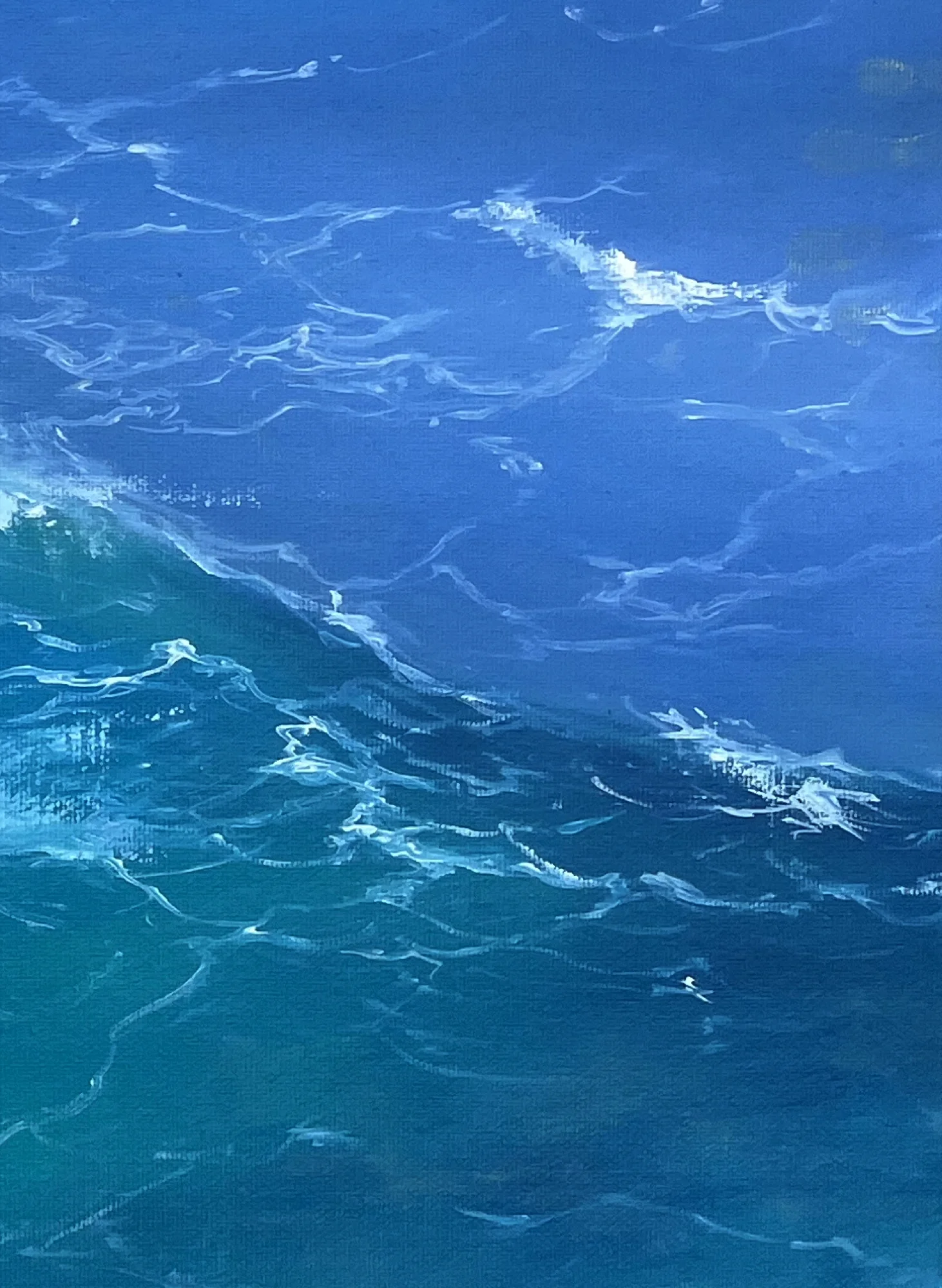 Close detail: deep blue open water above a teal swell, divided by a long diagonal of foam and fine spray